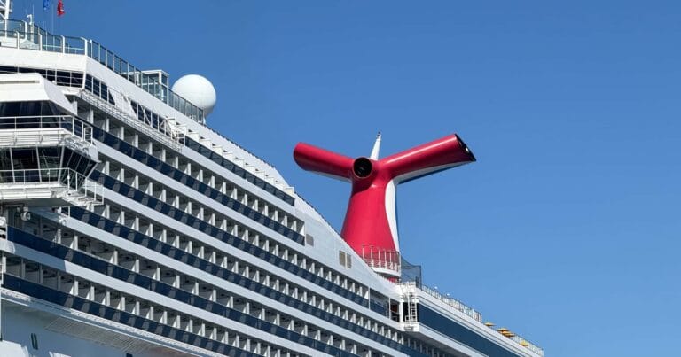 Red Carnival cruise ship funnel with balconies below and a clear blue sky.